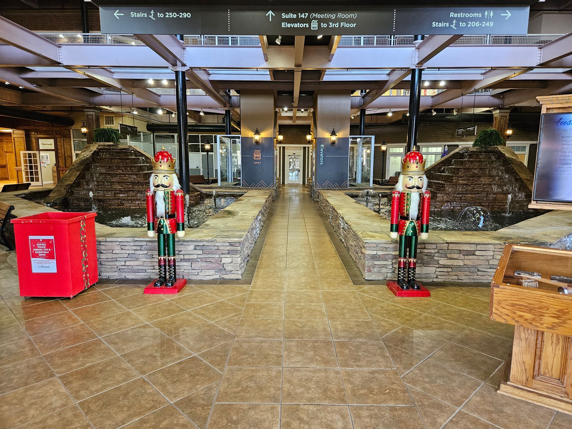Holiday-decorated indoor lobby with two nutcracker statues, stone planters, and a red recycling bin