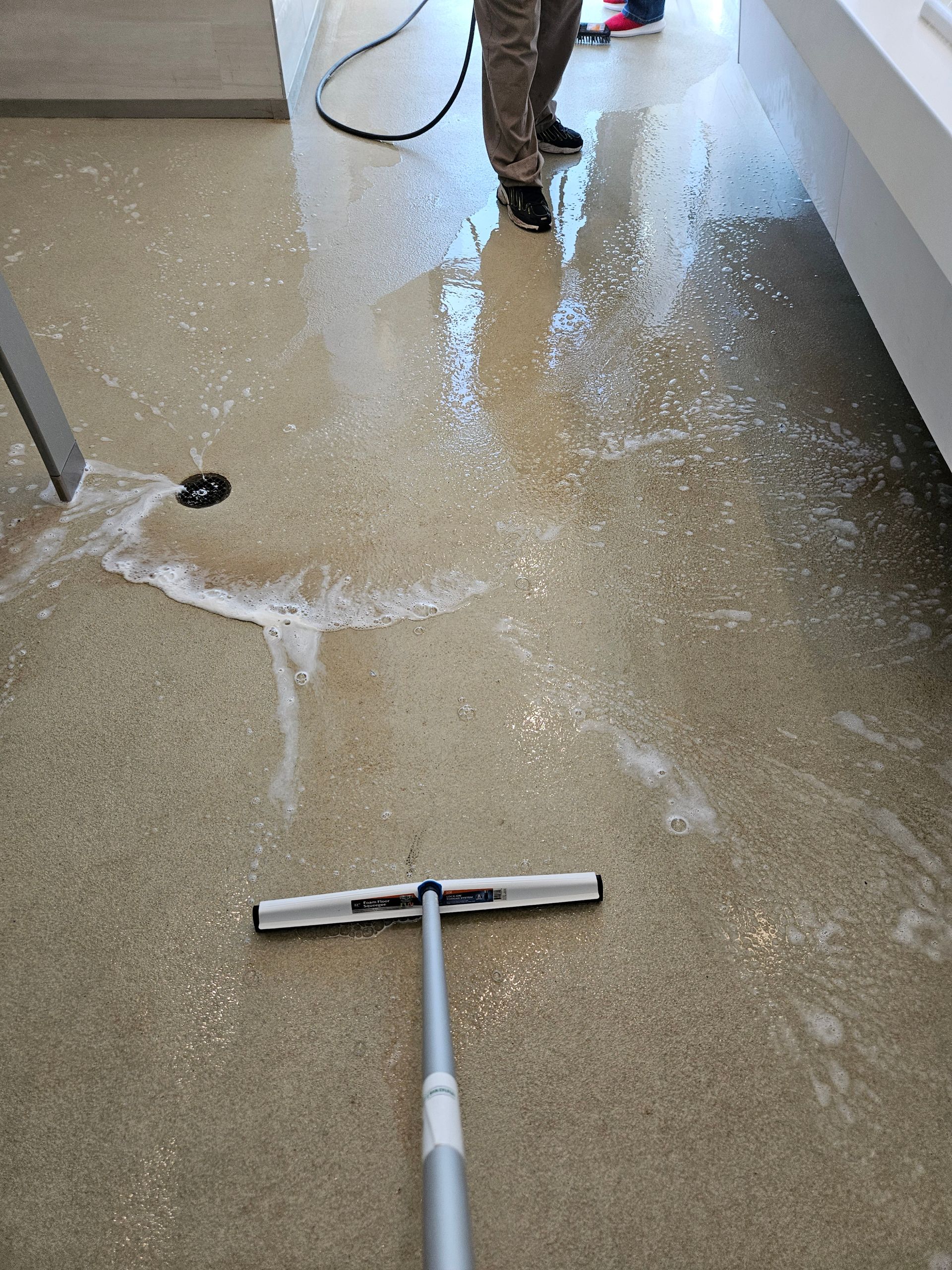 Flooded hallway being cleaned with a floor squeegee; water spread across the floor.