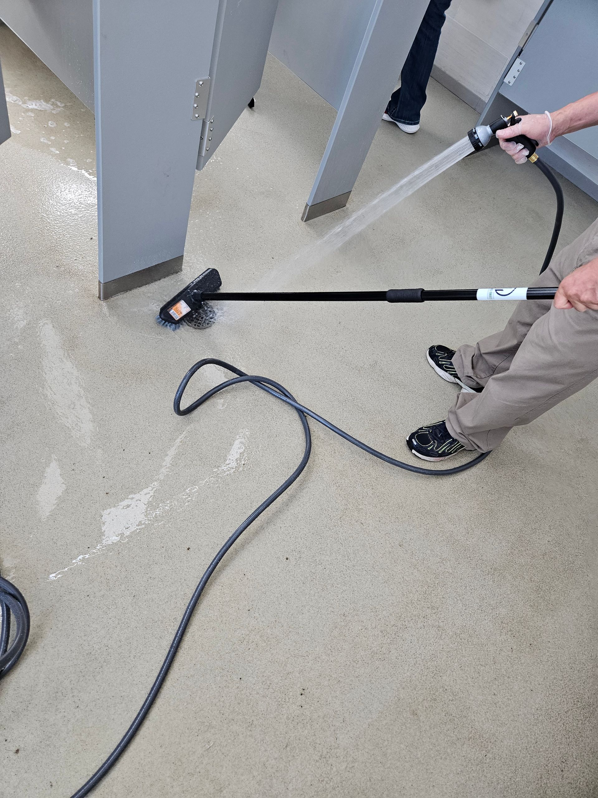 Person using a pressure washer to clean a concrete floor around metal supports.