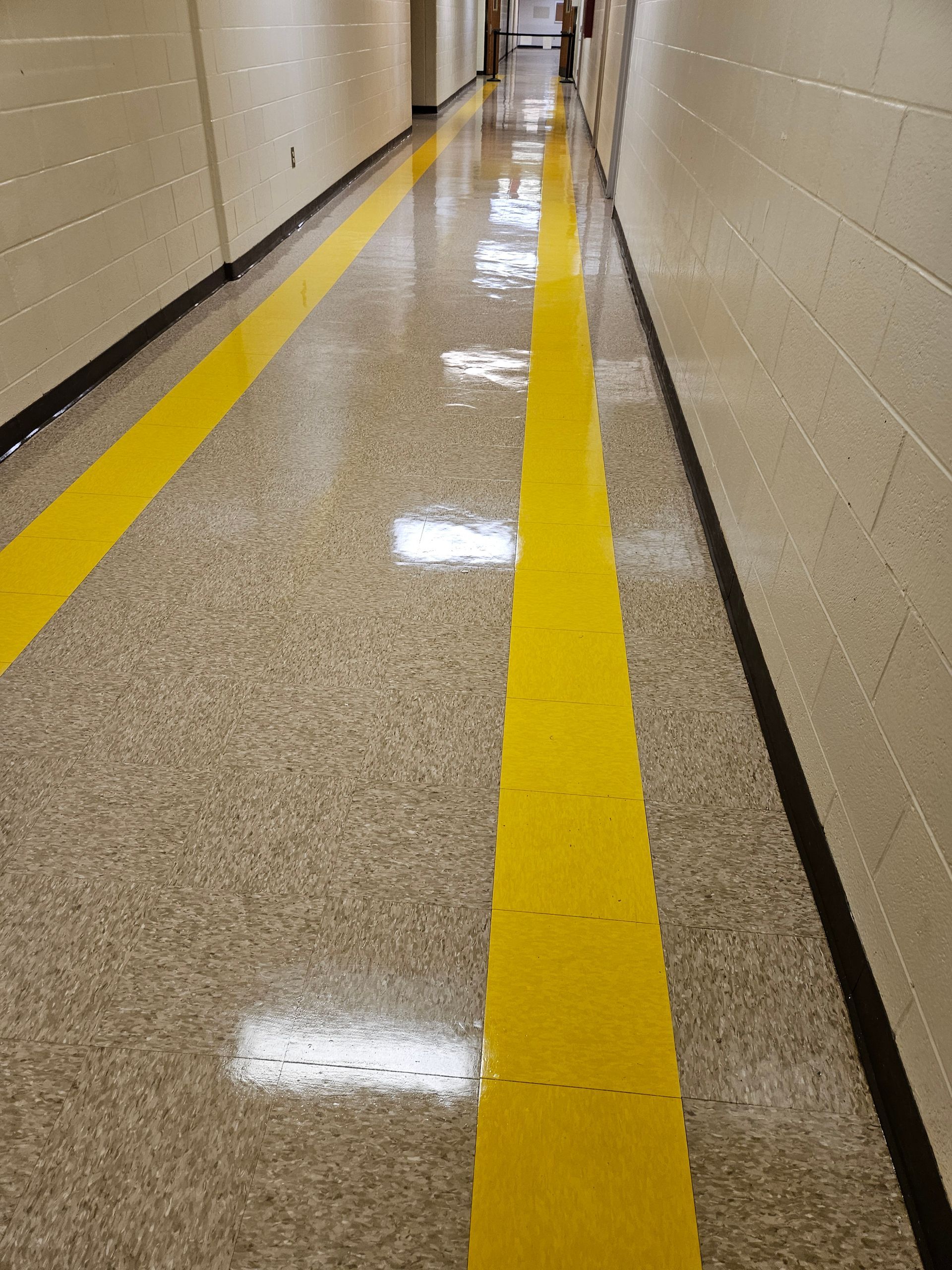 Narrow hallway with beige walls and bright yellow floor guide lines on a shiny speckled floor.