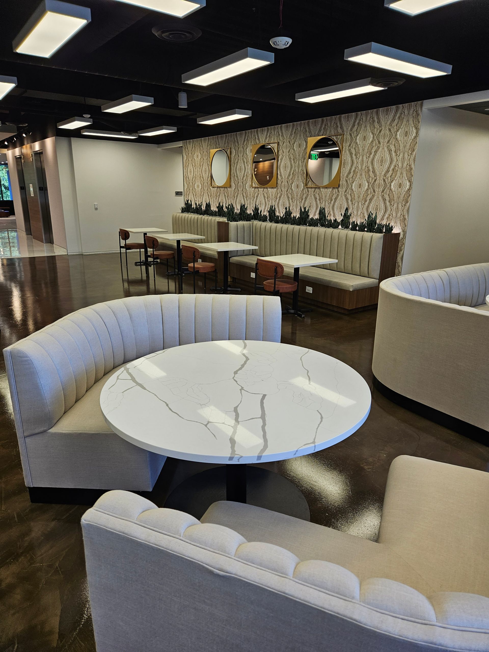 Modern lounge seating with white round tables, curved sofas, and mosaic wall decor in a sleek interior