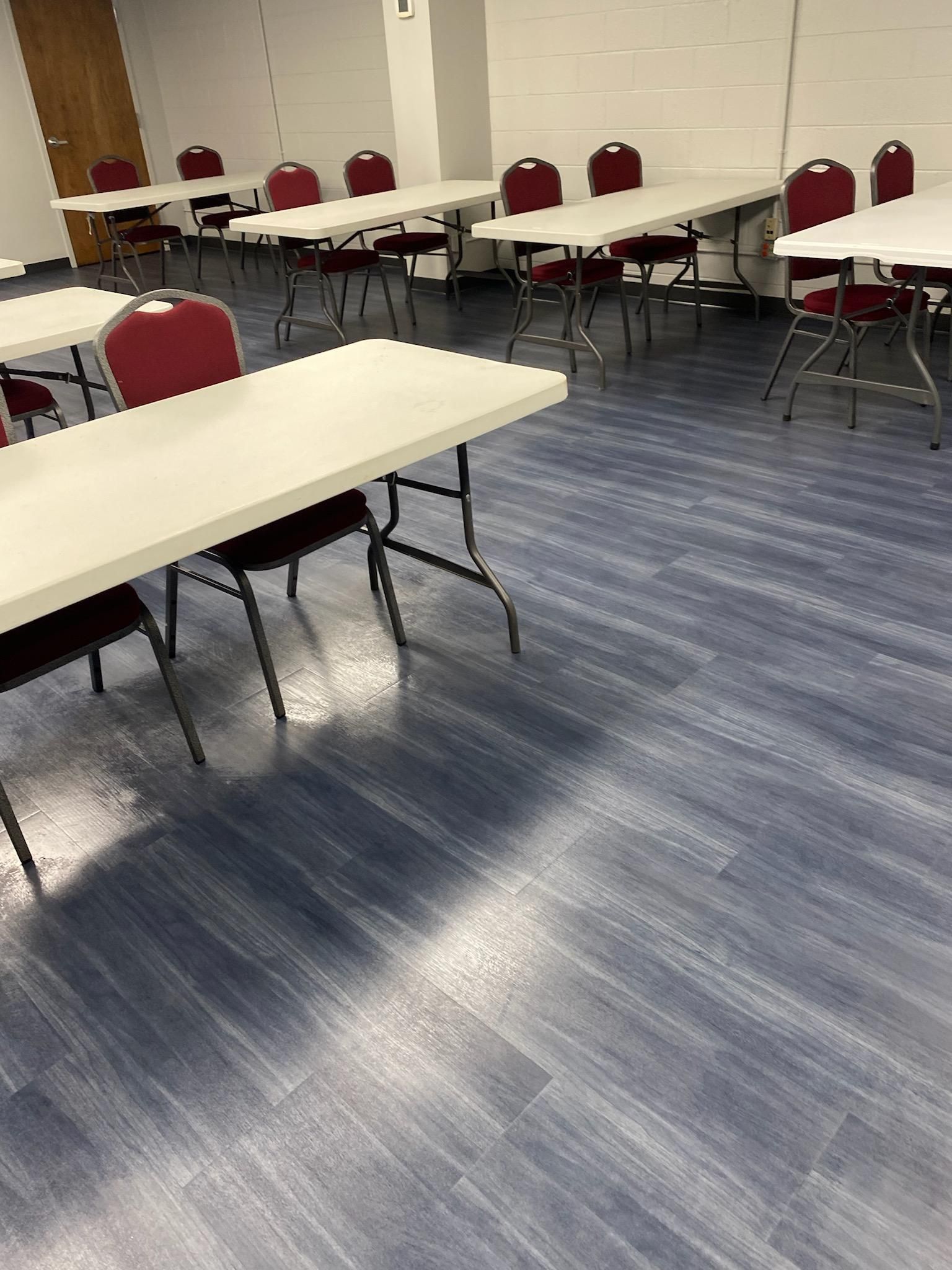 Empty meeting room with white tables, red chairs, and blue carpet.