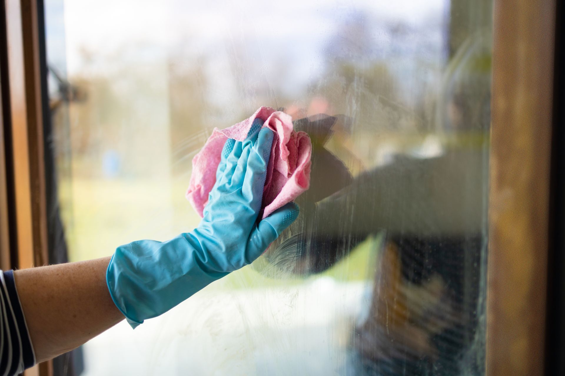 Hand in blue glove wiping a window with a pink and blue cloth