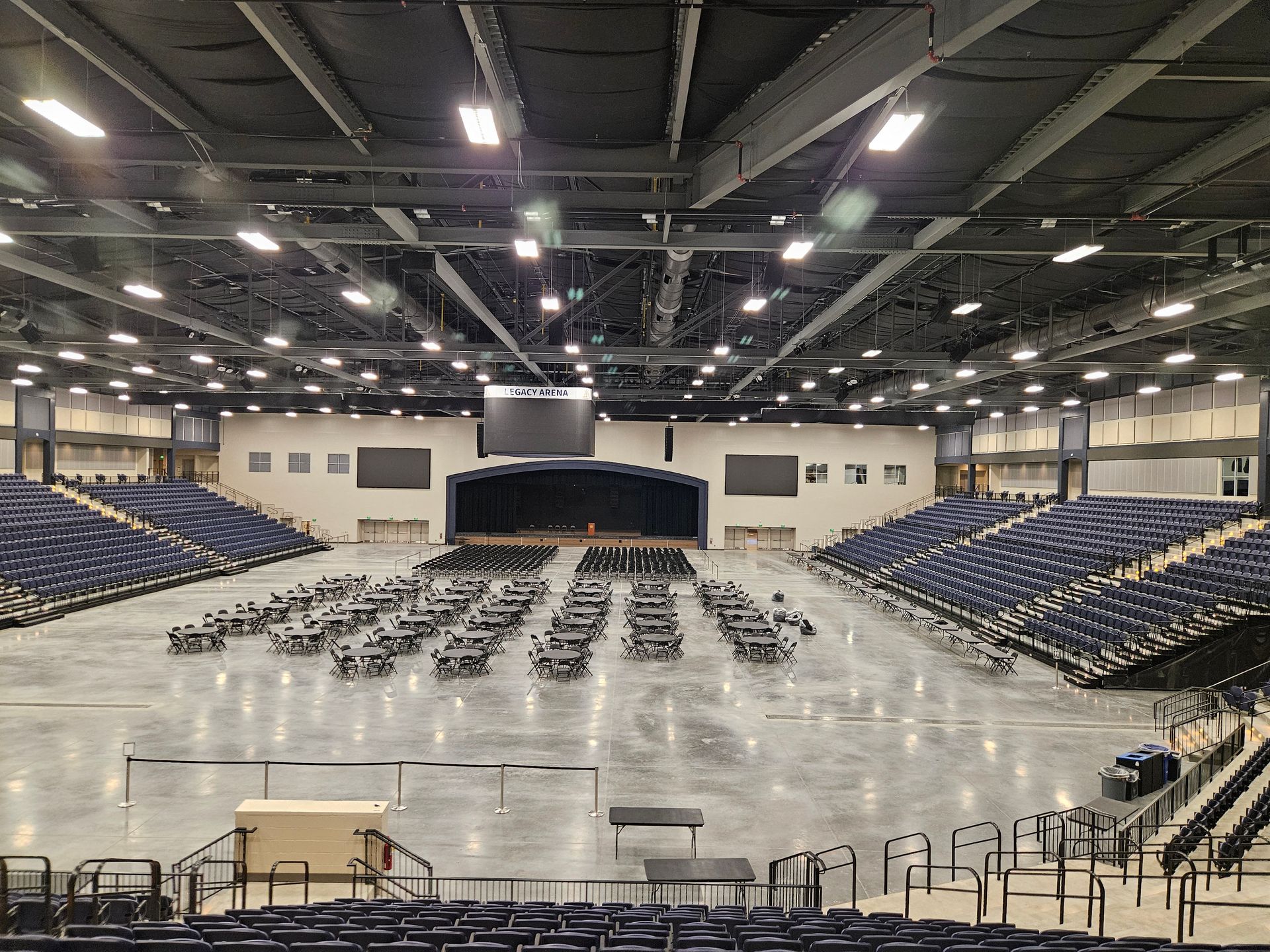Indoor arena with rows of folding chairs facing a stage and giant screen, empty and ready for an event