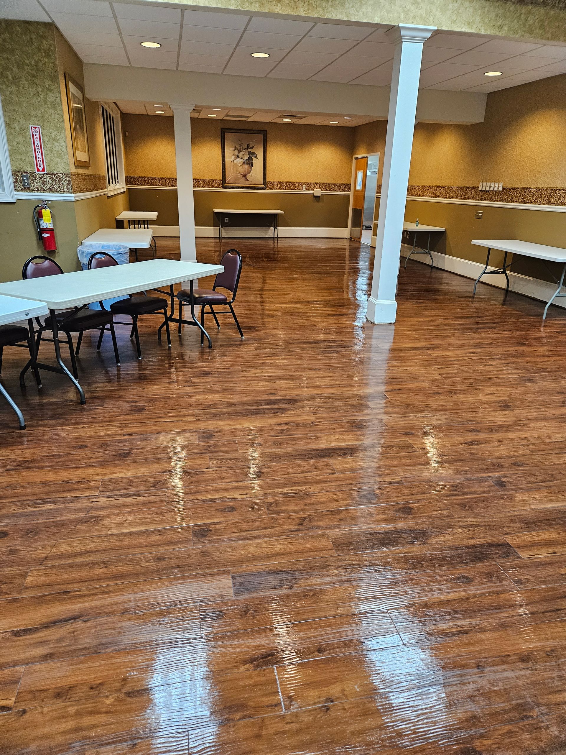 Banquet room with tables, white tablecloths, and a polished wood floor reflecting lights and a central column