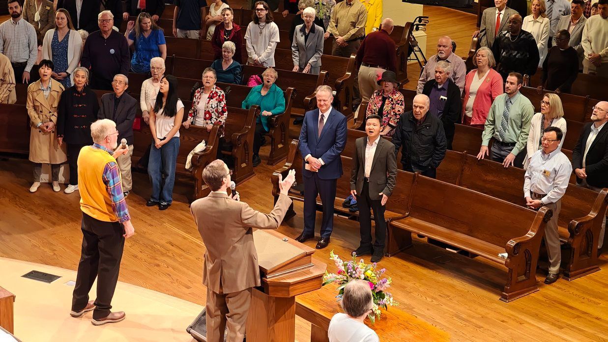 The congregation sings together, shown looking out at the pews. The pastors are in the front row and singers in the front.