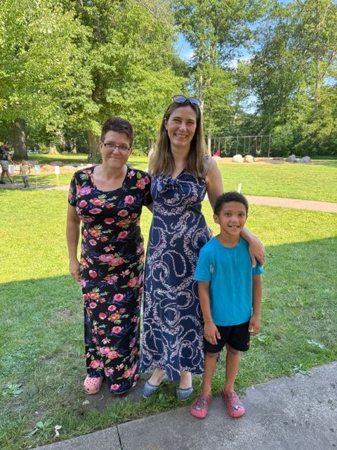 Three people standing on grass in a sunny park, posing for a photo.