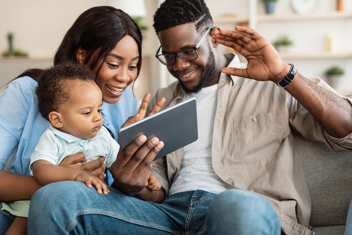 Family on a couch looking at a tablet, smiling and waving together