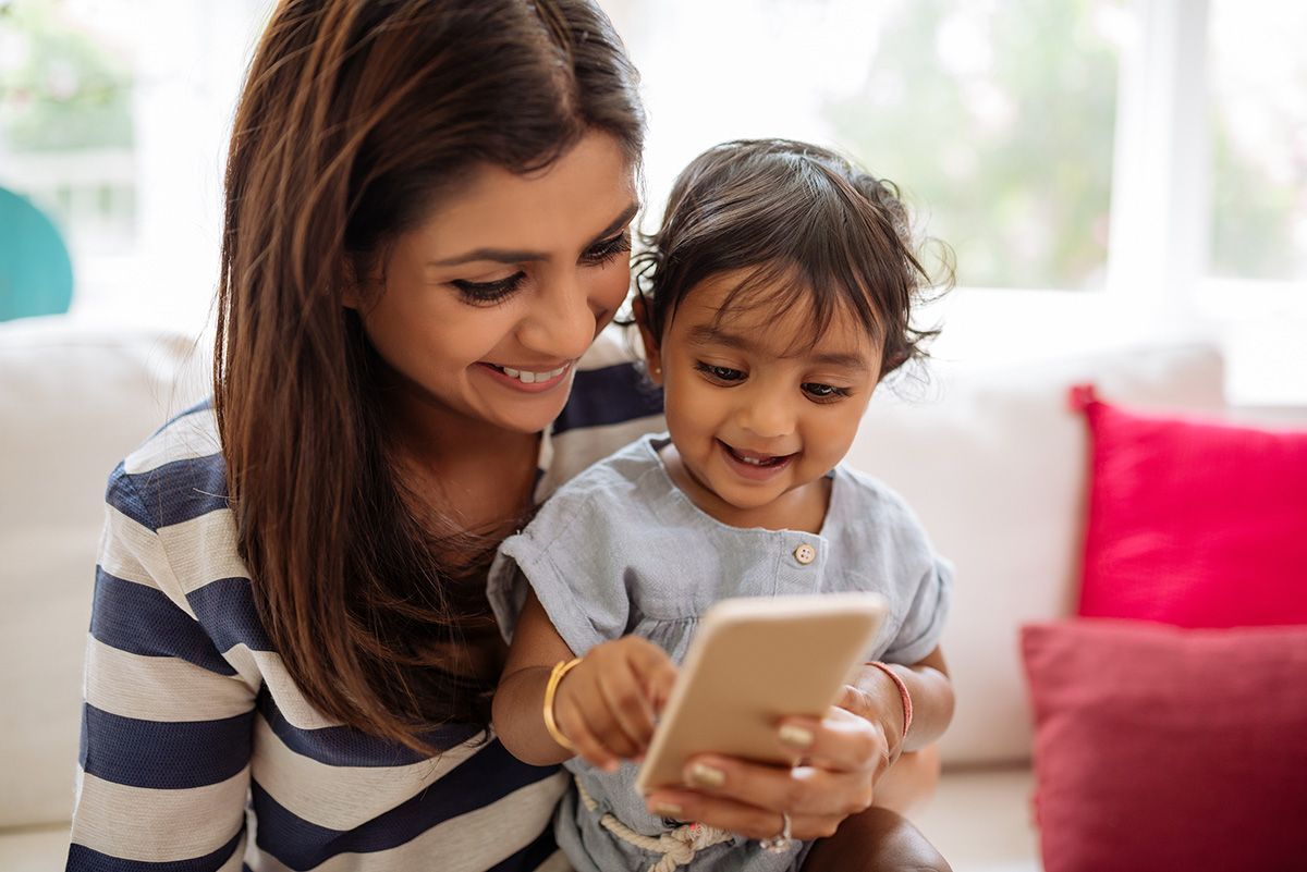 Woman and child smiling while looking at a smartphone on a couch