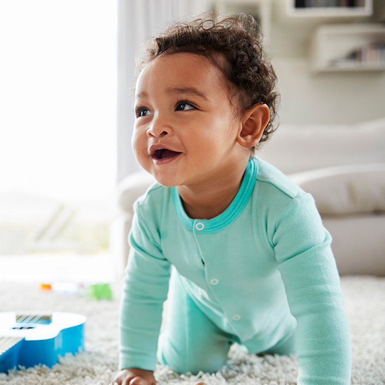Smiling baby in a teal onesie crawling on a soft rug indoors