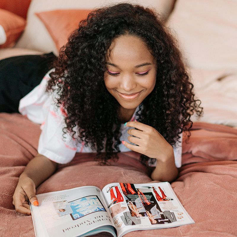 Person smiling and reading a magazine on a bed with peach bedding