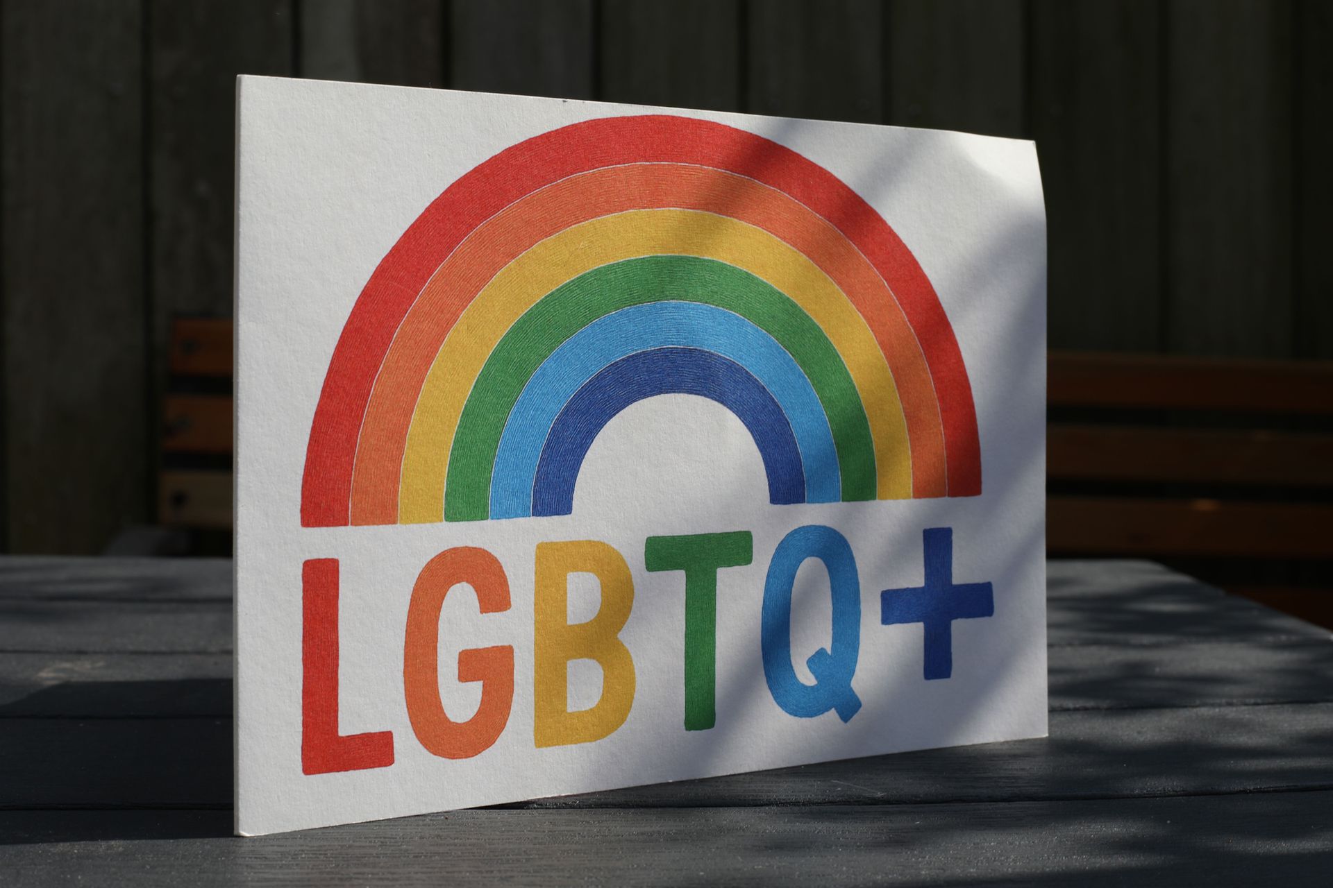Sign with rainbow and LGBTQ+ text on a table.