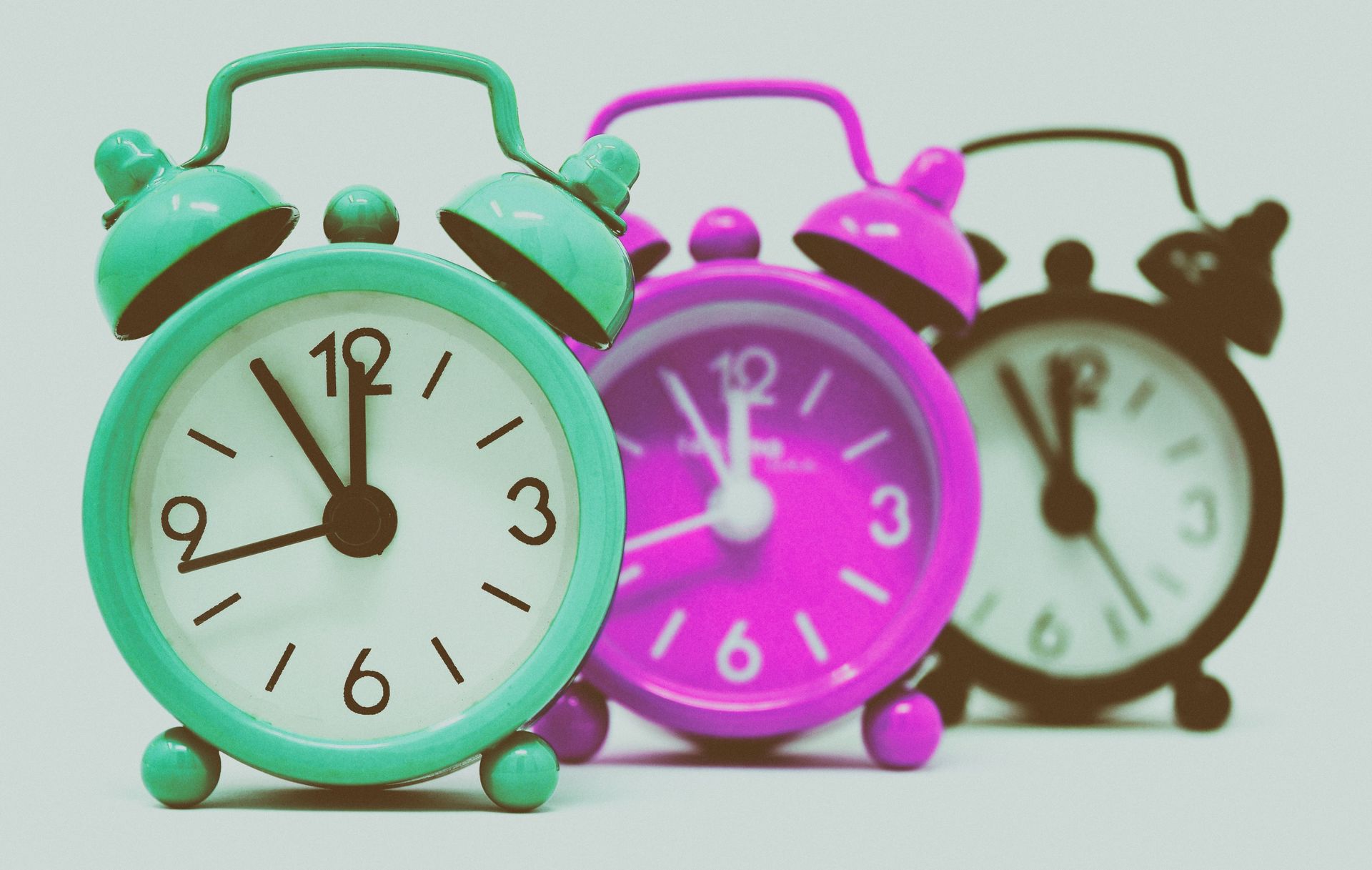 Three colorful alarm clocks lined up, with mint green in front and pink and brown behind
