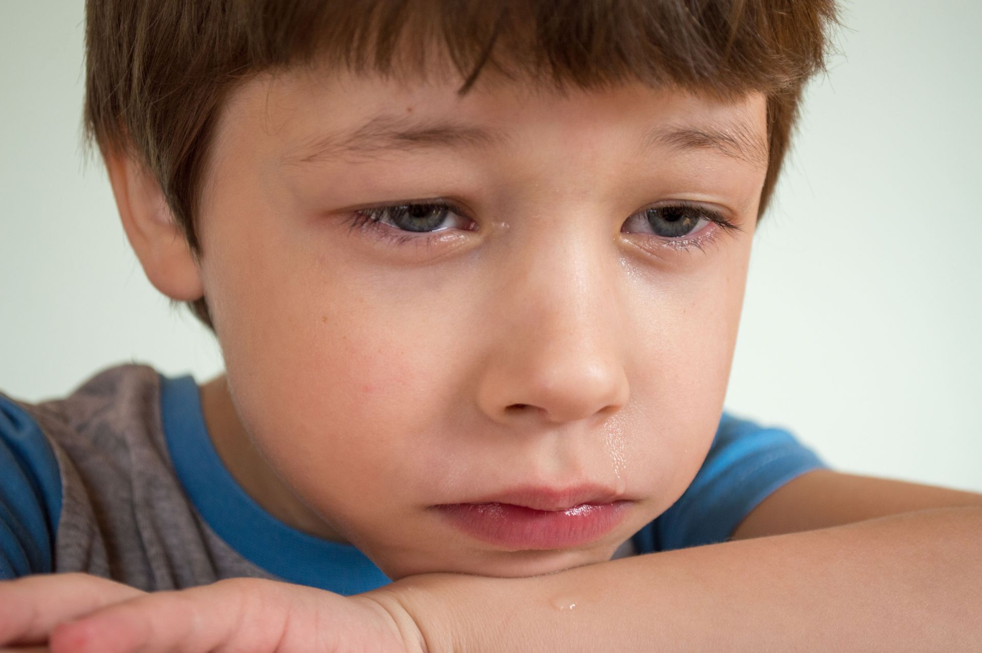 Sad child resting his head on folded arms, looking down thoughtfully.