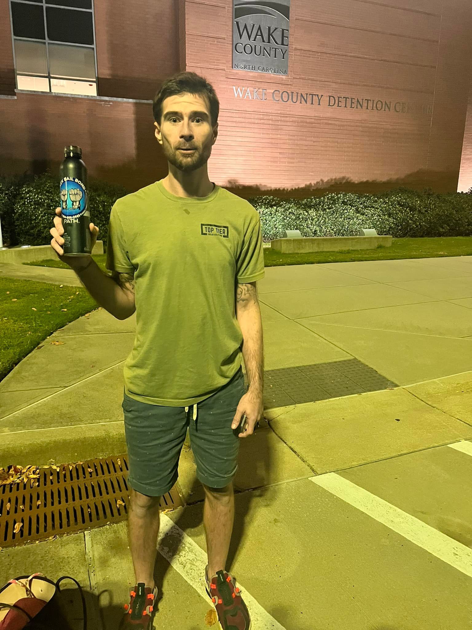 A man is standing on a sidewalk holding a bottle of water.