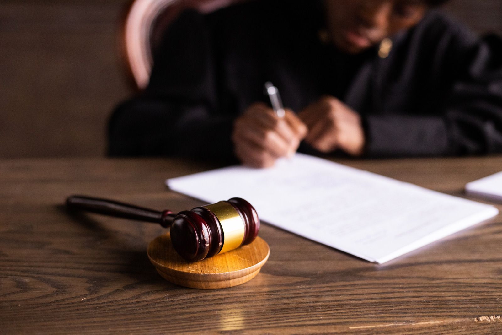 Wooden gavel on block; person in robe writing on a document.