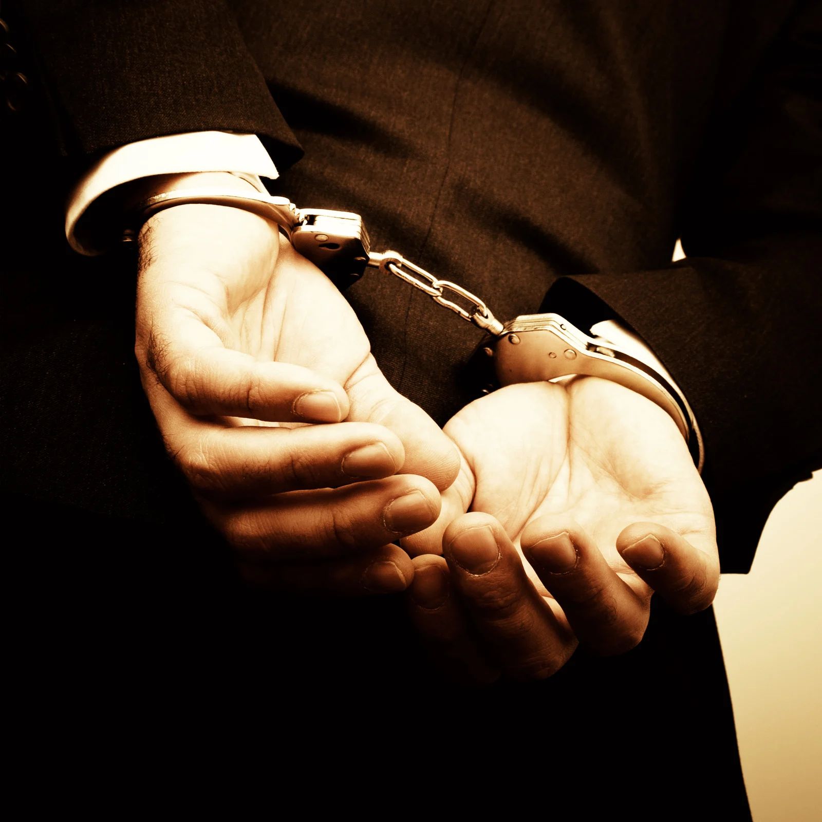 Handcuffed hands in a dark setting, wrists bound with metal cuffs and chain.