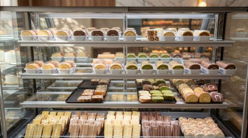 Bakery display case filled with assorted pastries, cakes, and sandwiches on metal shelves
