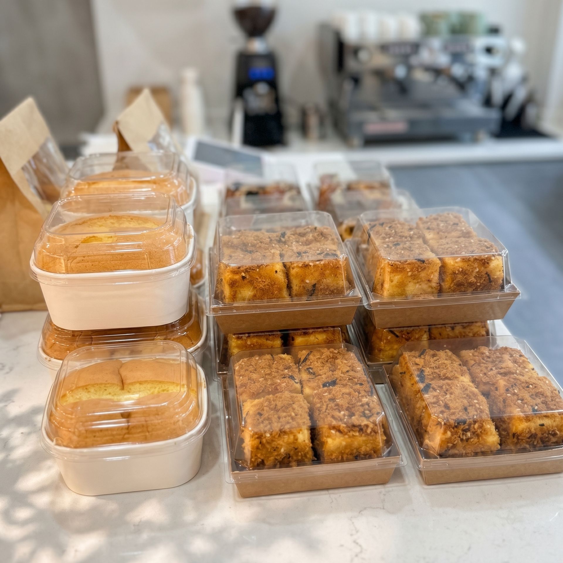 Trays of assorted baked goods and wrapped loaves displayed on a counter in a kitchen or bakery.