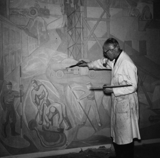 En man i labbrock målar en väggmålning på en vägg