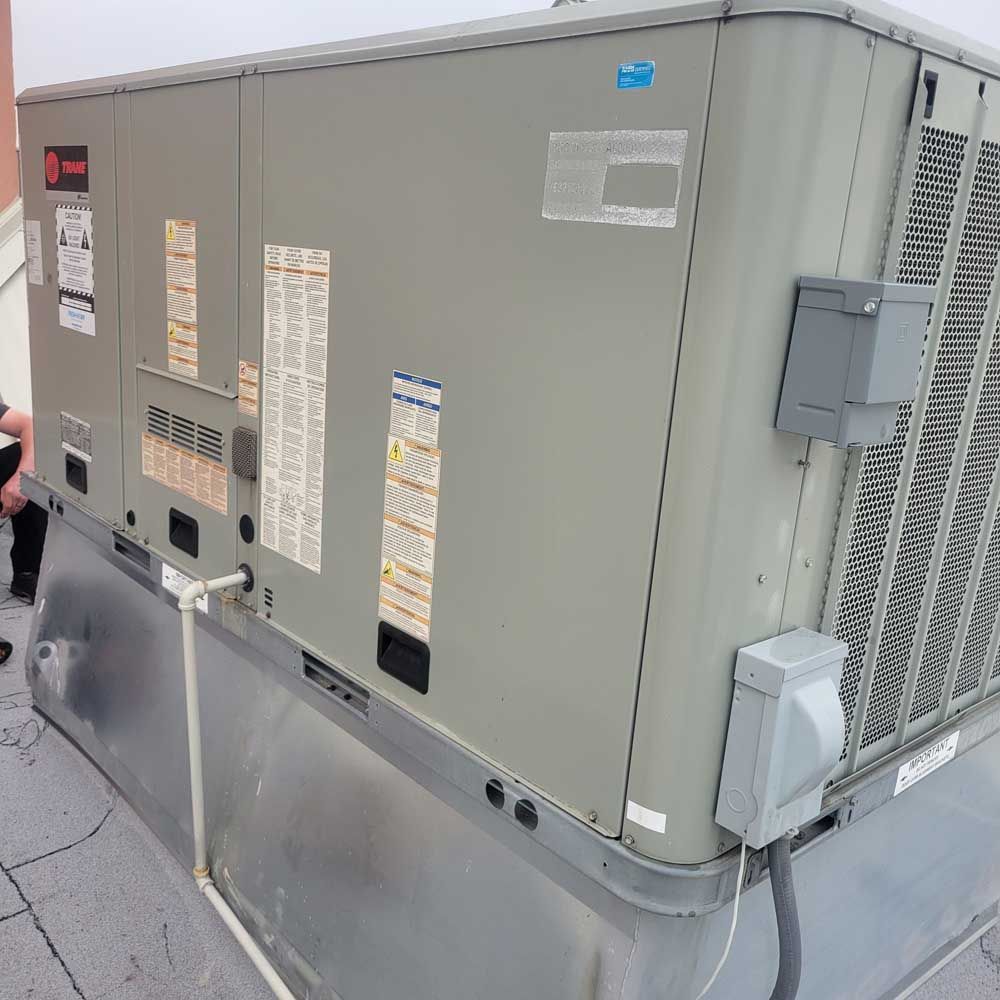 Gray rooftop HVAC unit with vents, service panels, and conduit on a commercial building roof