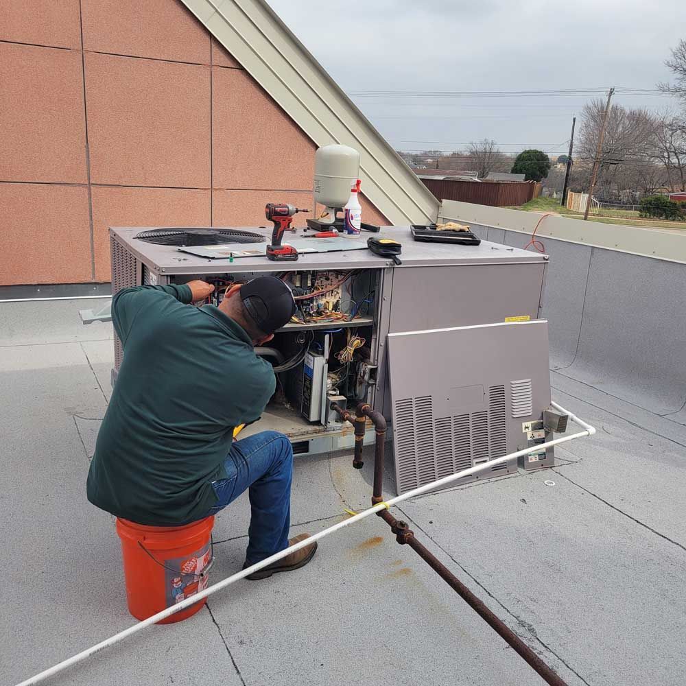 Technician repairing rooftop HVAC unit beside a peach-colored building