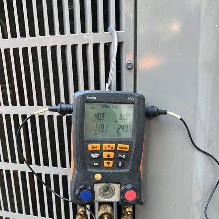 Handheld meter with display and buttons connected to an HVAC unit’s vent and side panel