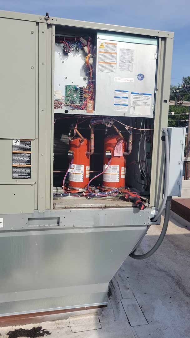 Open electrical cabinet with two orange fire extinguishers inside, outdoors near a building.