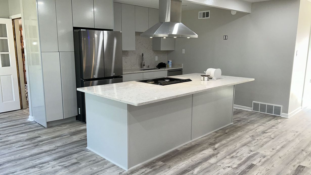 A modern kitchen featuring light gray cabinets, a large white-topped island with a stovetop, and stainless steel appliances.