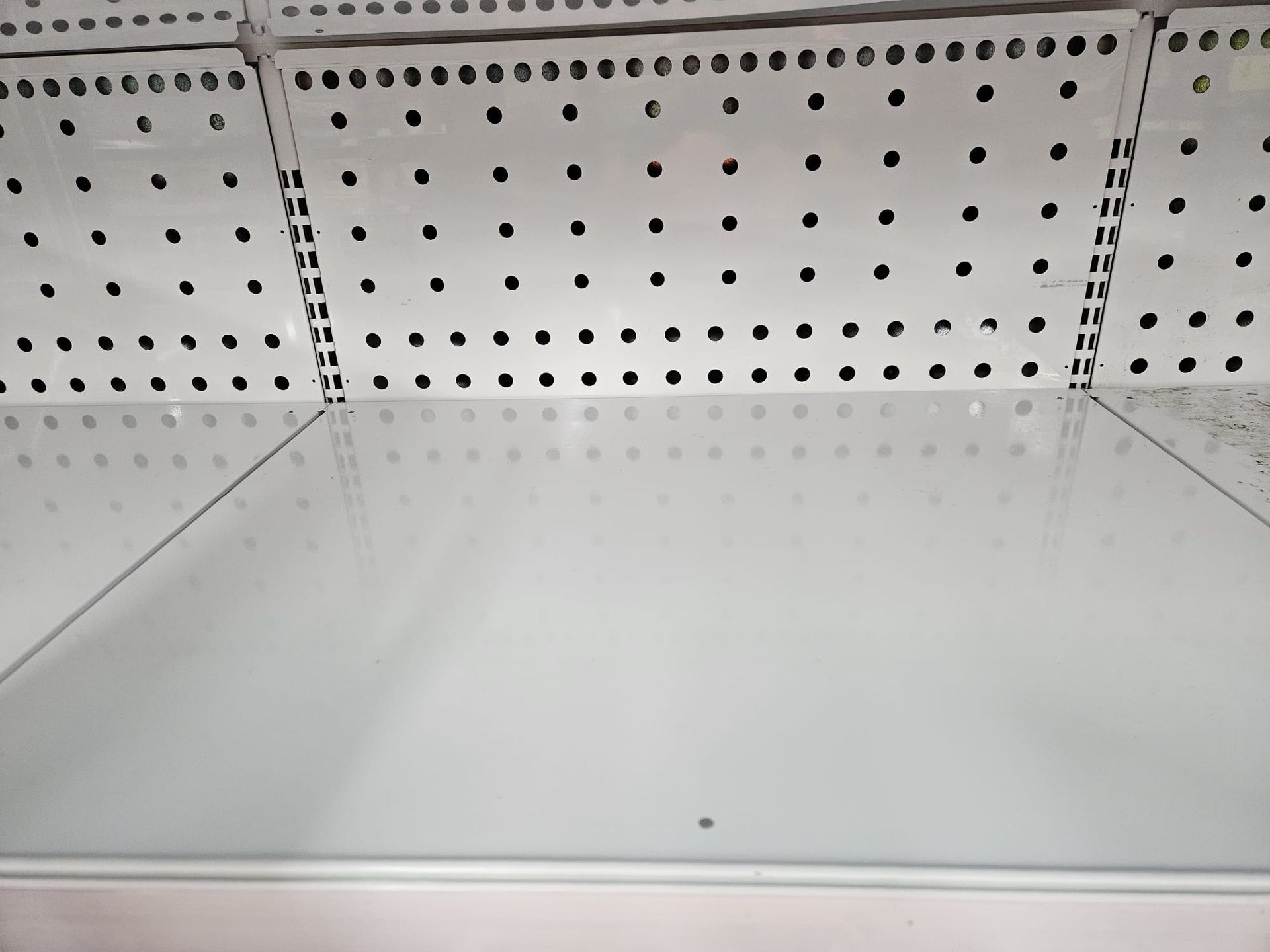 An eye-level shot of an empty white retail store shelf with a perforated metal back panel.