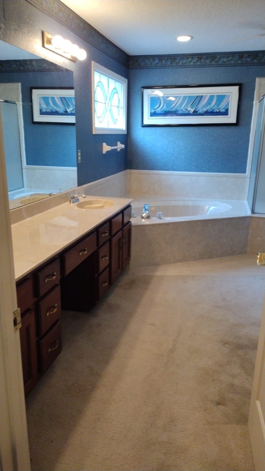 A bathroom with blue walls, a long vanity with dark wood cabinets, a large mirror, and a corner soaking tub.