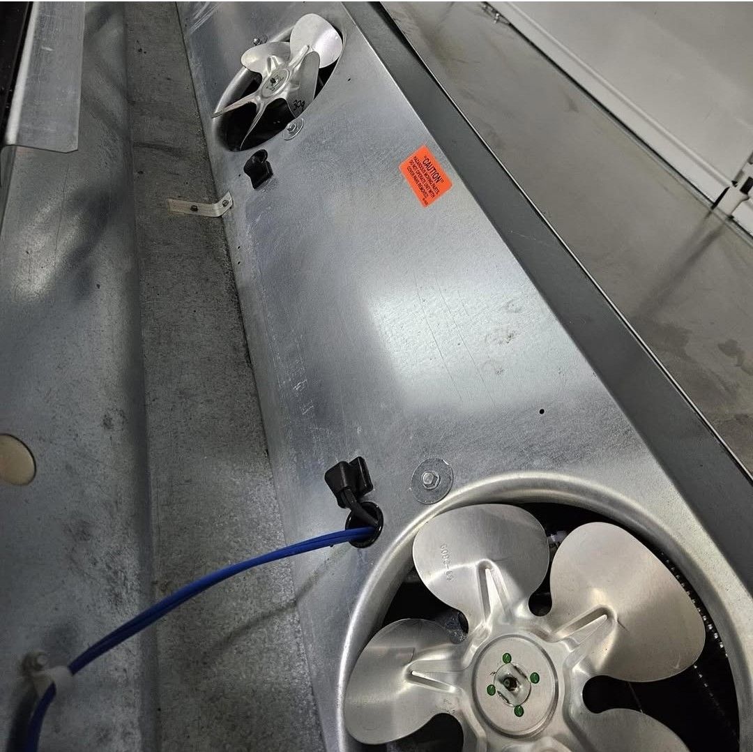 Two metal cooling fans mounted on a silver industrial refrigeration unit, with a blue wire connected to one.