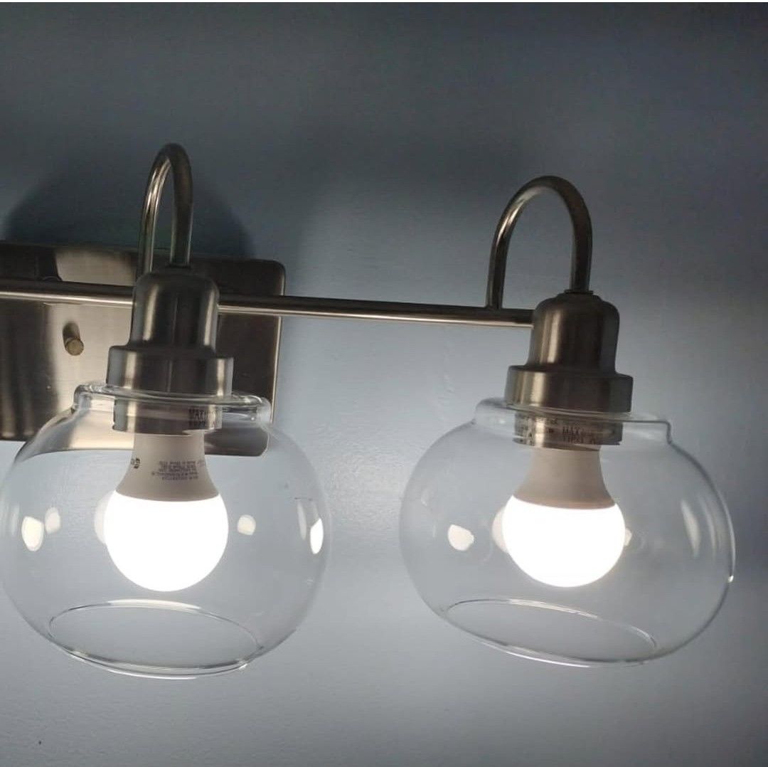 Two illuminated glass-globe vanity lights with a brushed nickel finish mounted on a blue wall.
