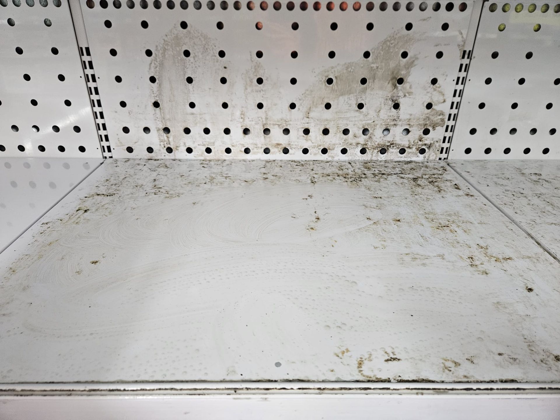A white, metal retail display shelf and pegboard back panel showing significant dirt, grime, and debris.