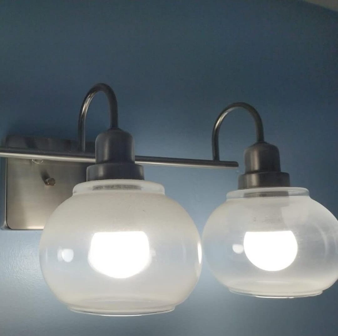 A two-light wall vanity fixture with frosted glass globes and a brushed nickel finish against a blue wall.
