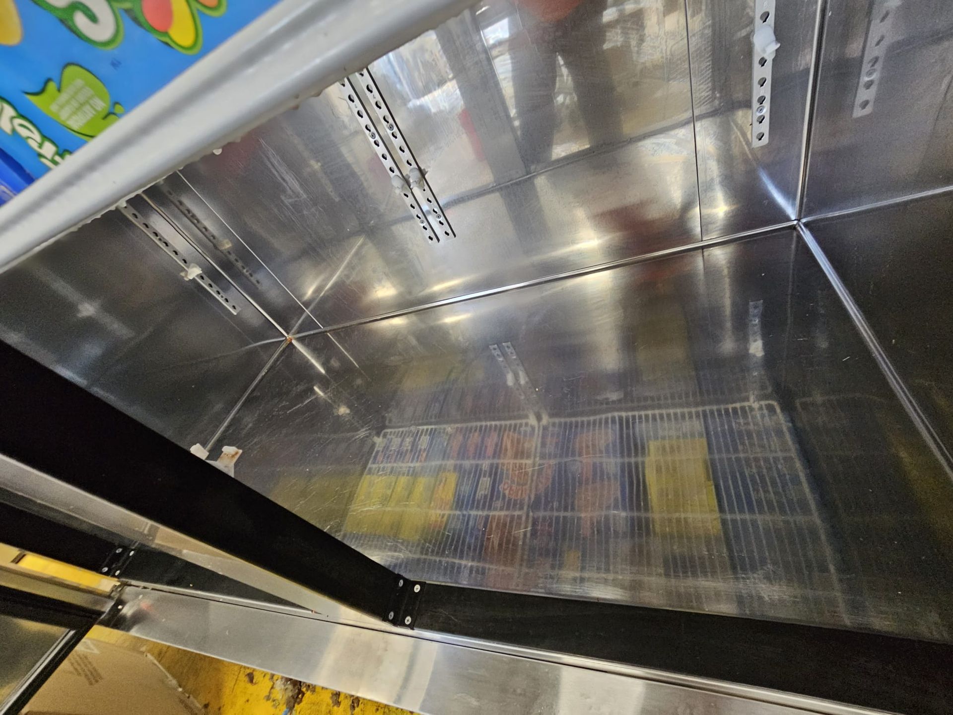 A high-angle view inside an empty commercial refrigerator with metal shelving and walls, showing light reflecting inside.