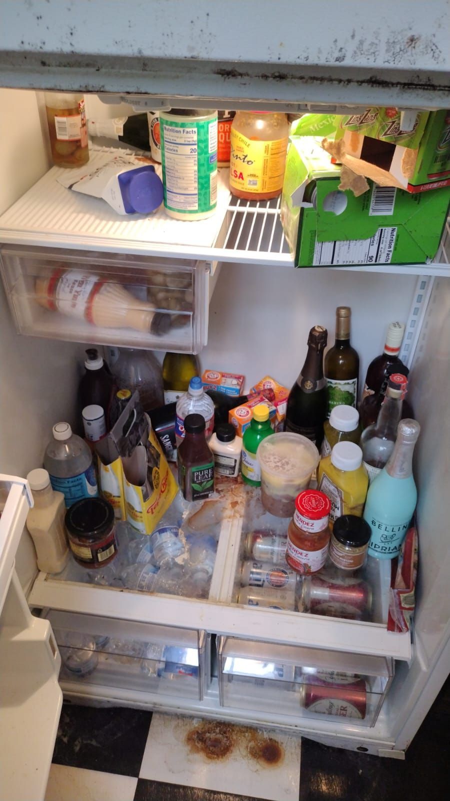 A cluttered refrigerator interior with two shelves and drawers, packed with various bottles, jars, and food containers.