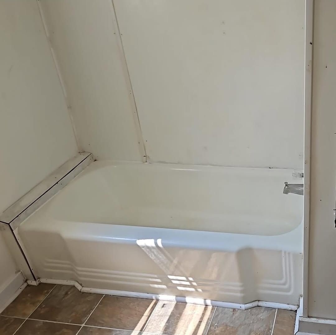 A white bathtub set against plain white walls in a bathroom with tiled flooring.