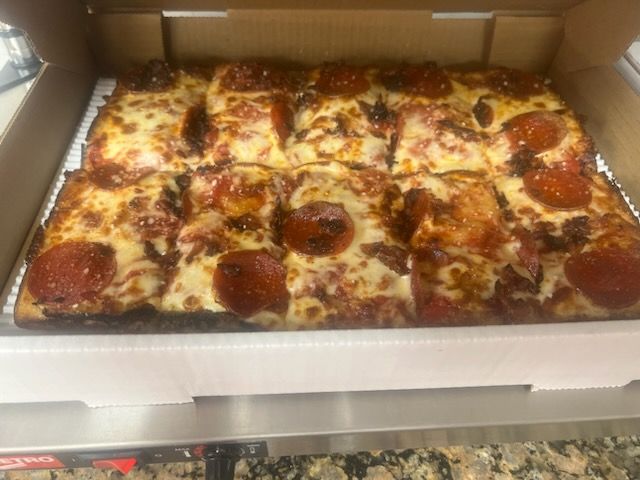 A pepperoni pizza is sitting in a cardboard box on a counter.
