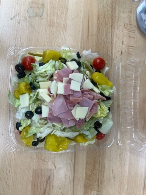 A salad in a plastic container on a wooden table.