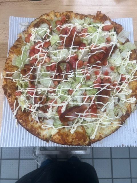 A pizza with lettuce tomatoes and bacon on it