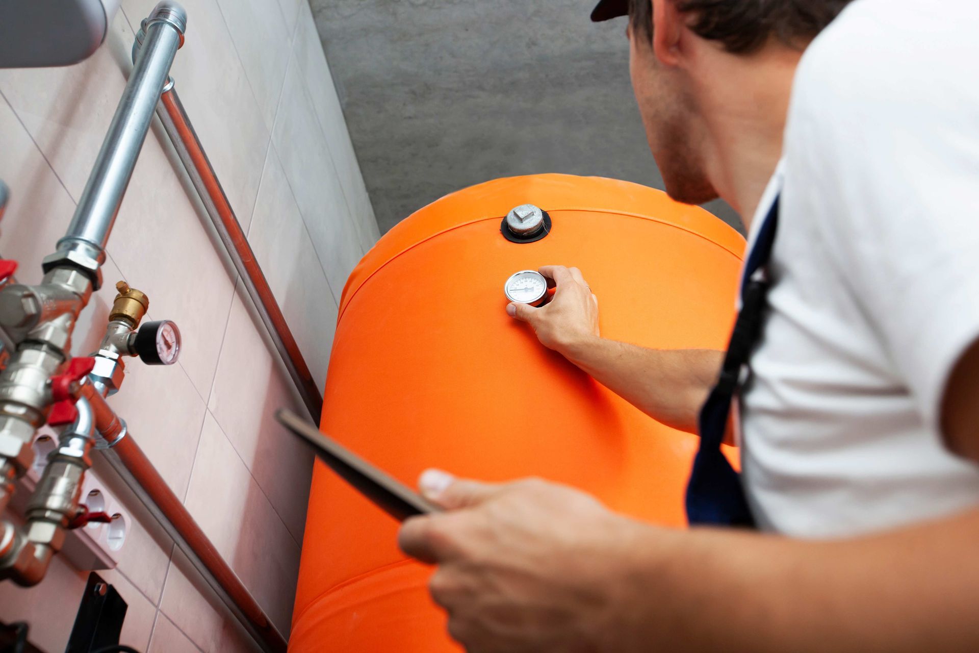 A home boiler contractor checks a gauge on a large orange boiler tank safely. A home boiler contractor checks a gauge on a large orange boiler tank safely.