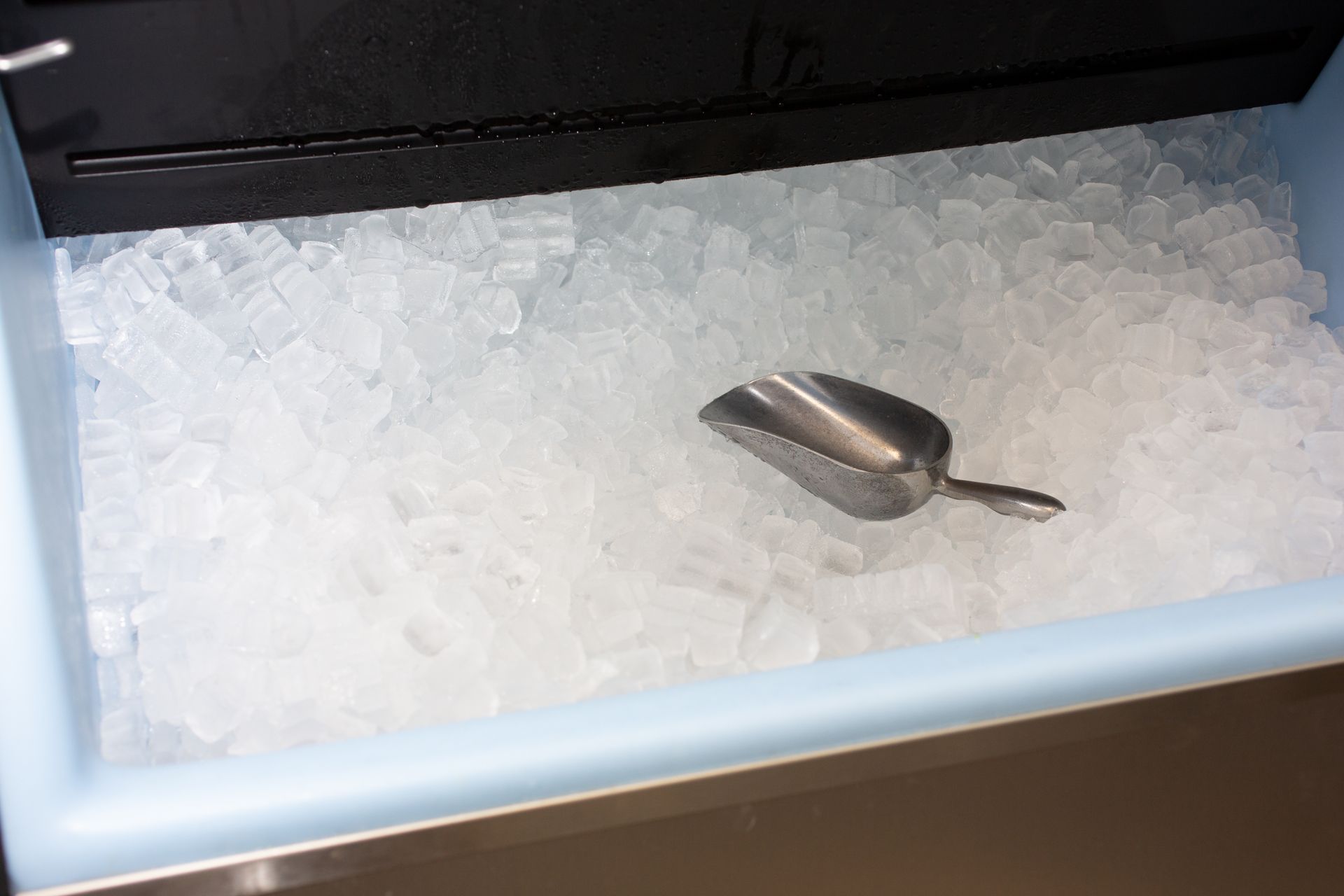 Metal scoop nestled in a fully stocked ice machine, surrounded by fresh ice.