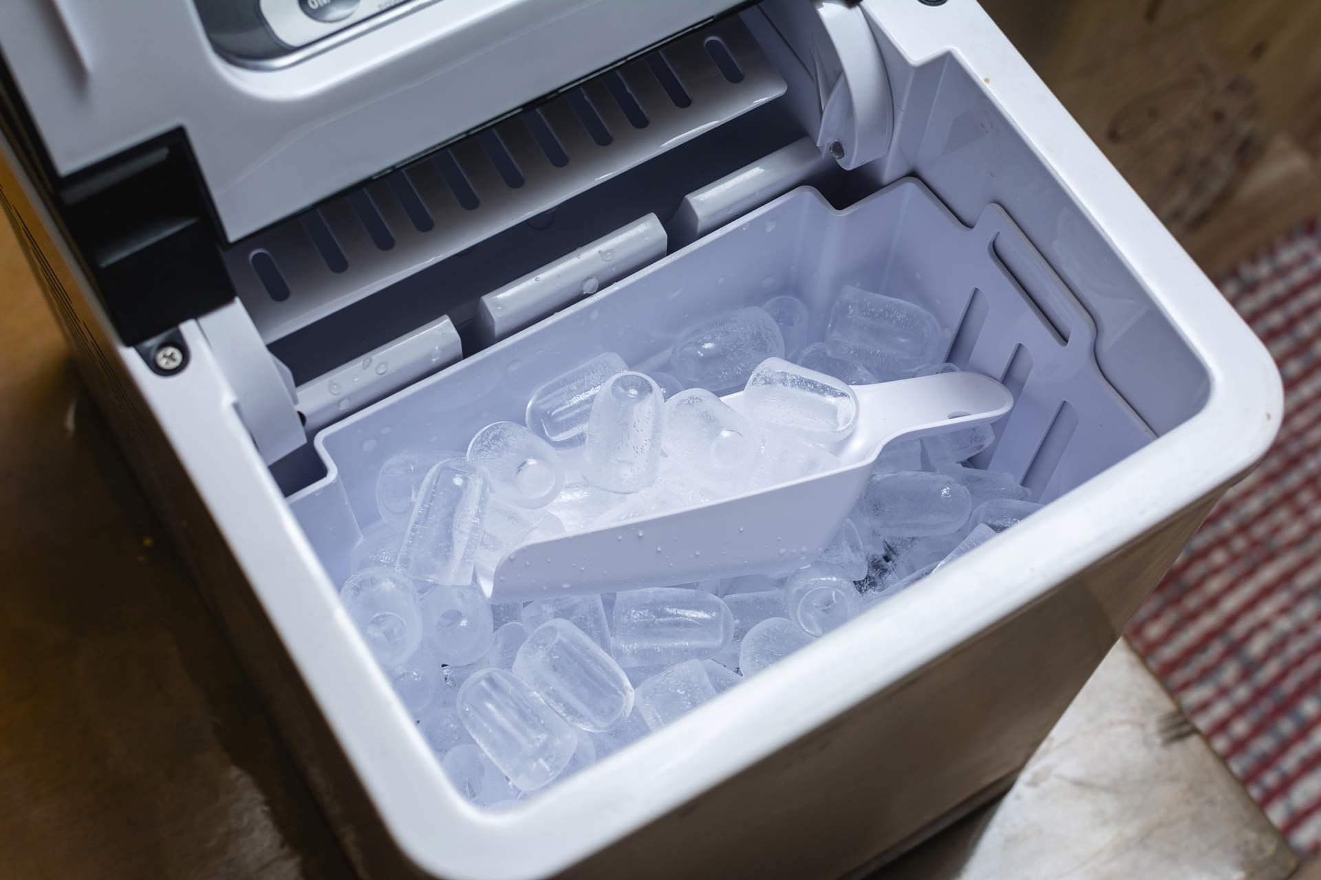 An ice maker with its lid open, revealing a bin full of ice cubes and a scoop.