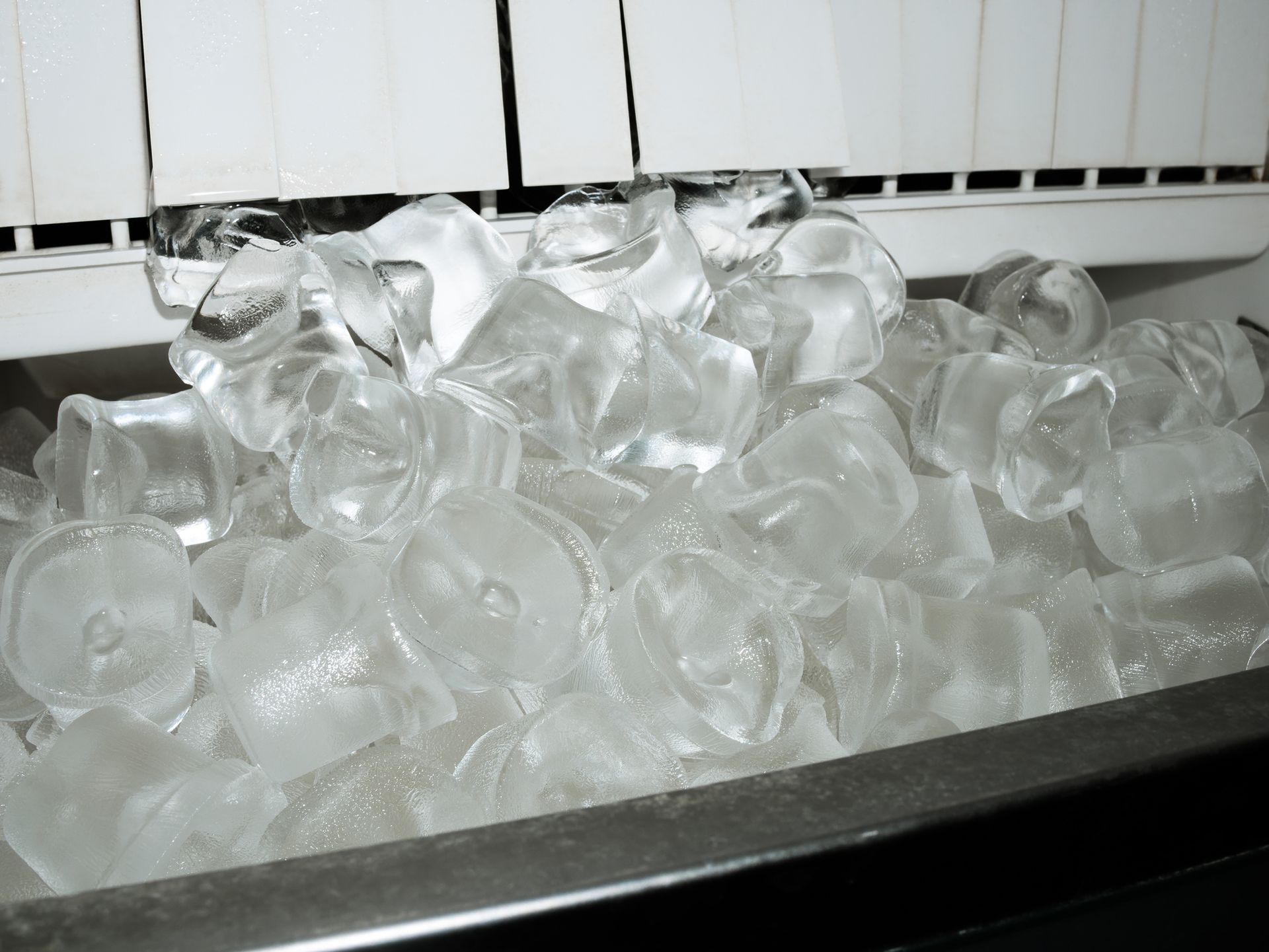A pile of molded ice cubes inside an open ice maker machine. A pile of molded ice cubes inside an open ice maker machine.