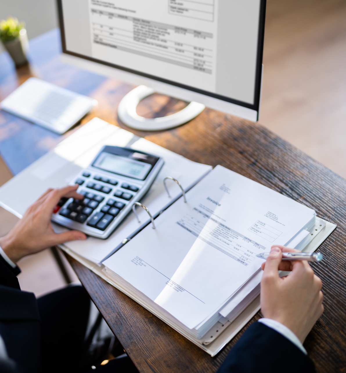 A person is using a calculator and a computer on a desk