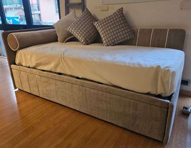 Divano letto estraibile con materasso beige chiaro e cuscini beige in un soggiorno.