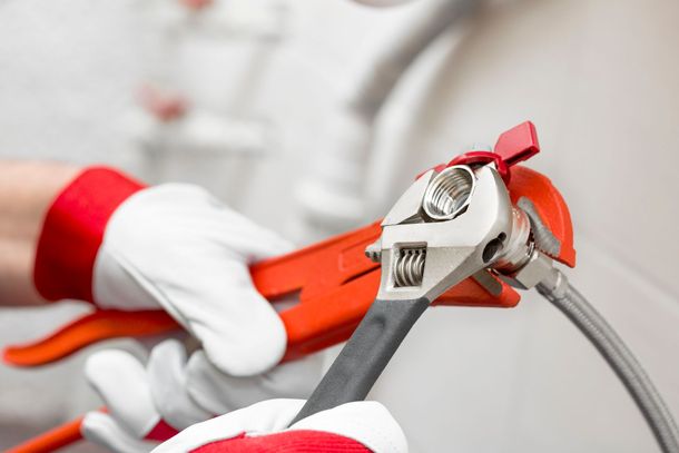 Gloved hands using an orange pipe wrench to tighten a metal pipe connection Gloved hands using an orange pipe wrench to tighten a metal pipe connection