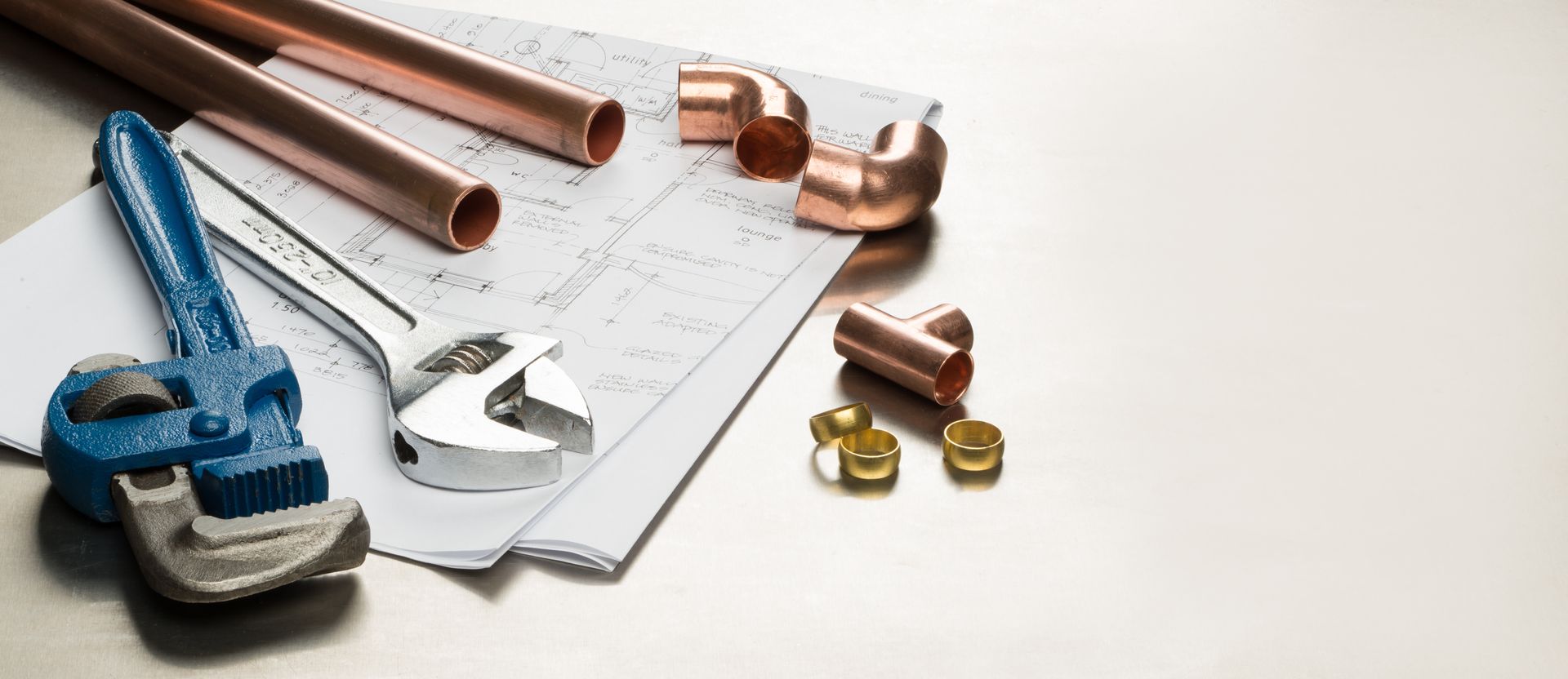 Plumbing tools, copper pipes, wrench, and fittings on a blueprint Plumbing tools, copper pipes, wrench, and fittings on a blueprint