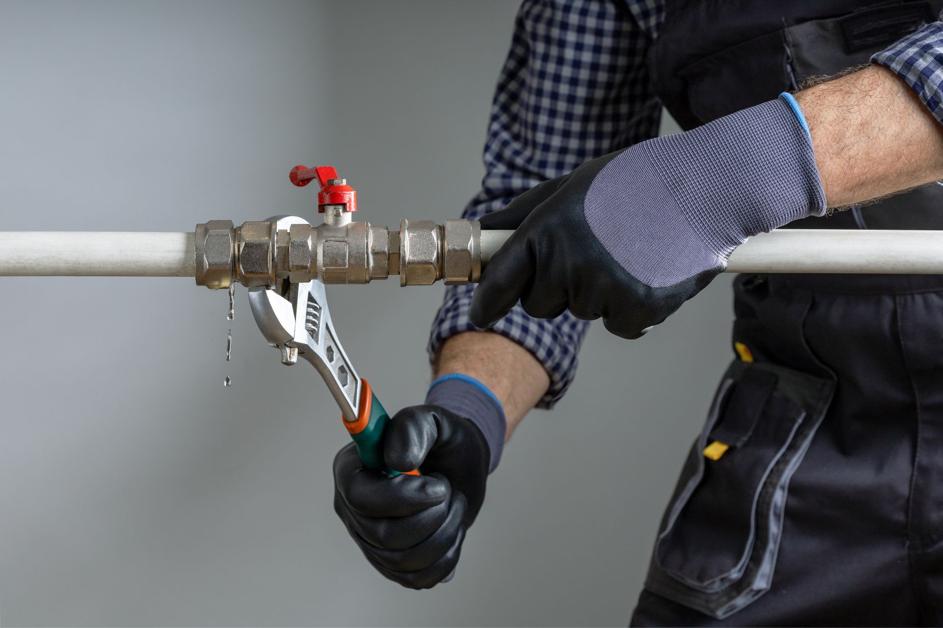 Gloved worker using pliers to adjust a metal pipe valve with red handle Gloved worker using pliers to adjust a metal pipe valve with red handle
